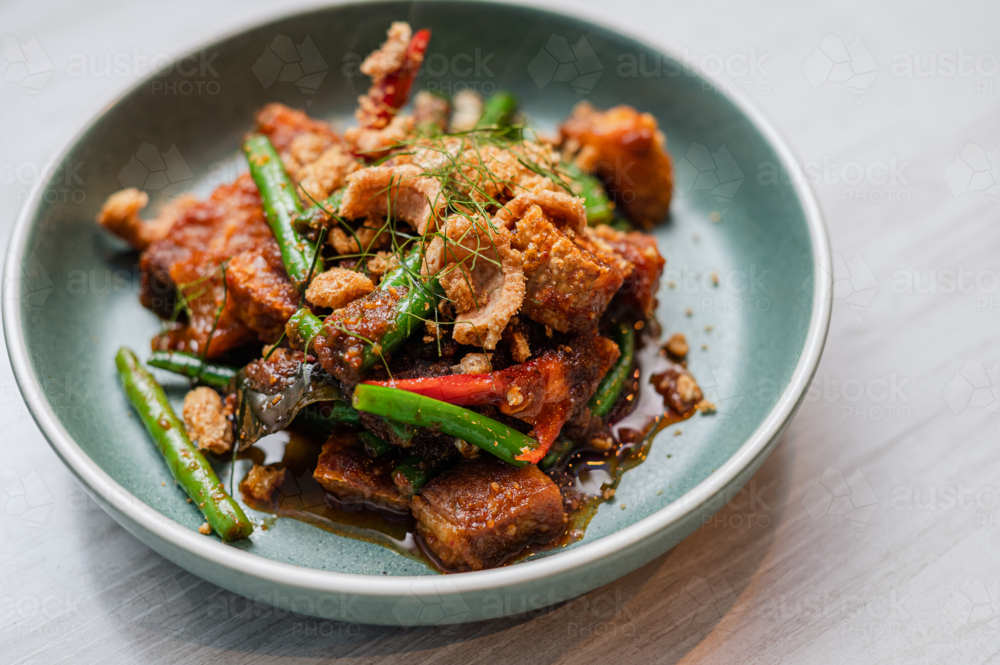 Stir-fried crackling pork belly, green beans, red peppers, and crispy garnishes - Australian Stock Image