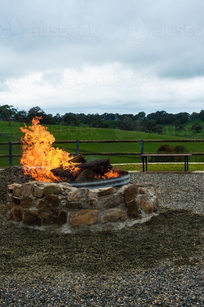 Stone outdoor fire pit with blazing fire - Australian Stock Image