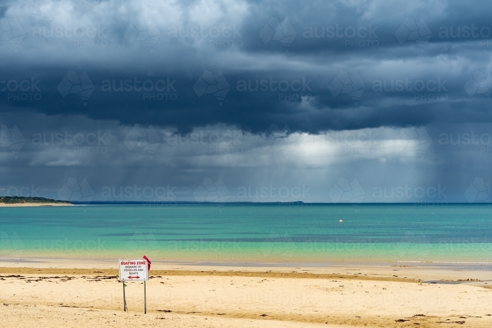Storm clouds and heavy rain falling over a calm ocean bay and deserted beach - Australian Stock Image