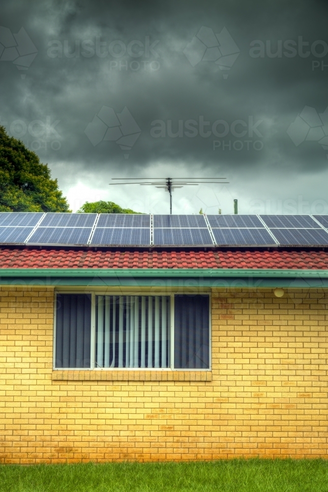 Storm clouds and suburban brick house with solar panels. - Australian Stock Image