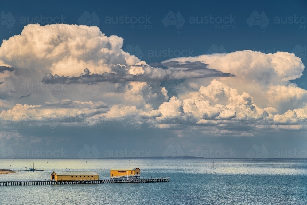 Storm clouds build over a jetty jutting out into the ocean - Australian Stock Image