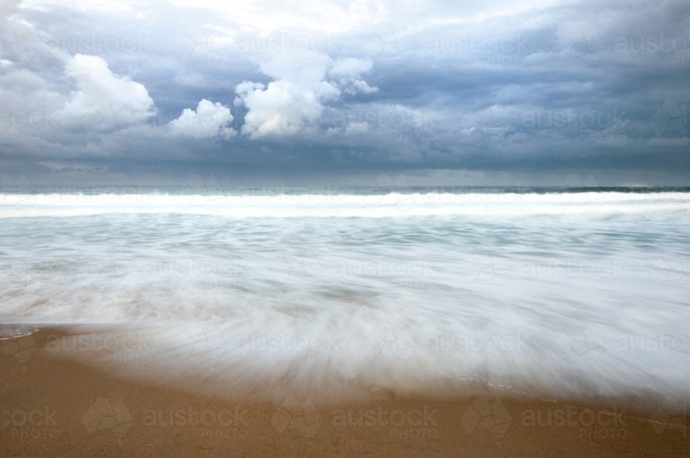 Storm clouds over a beach with blurred wave motion - Australian Stock Image