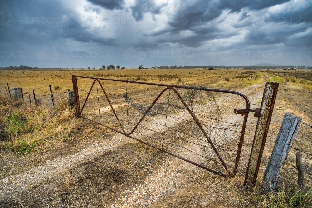 Storm clouds over an old rusty gate on dry farmland - Australian Stock Image