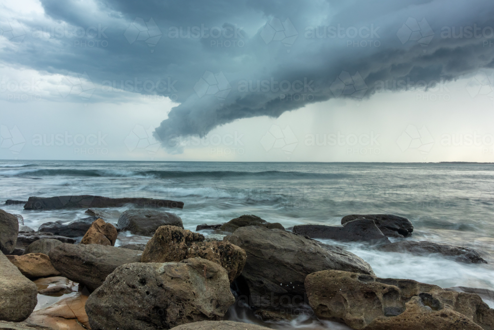 Storm clouds over ocean with rocky shoreline and waves - Australian Stock Image