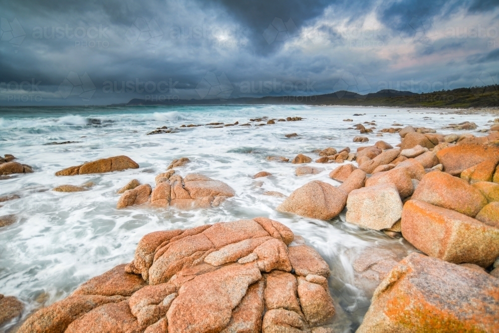Stormy clouds in the distance with rocks and ocean in the foreground - Australian Stock Image