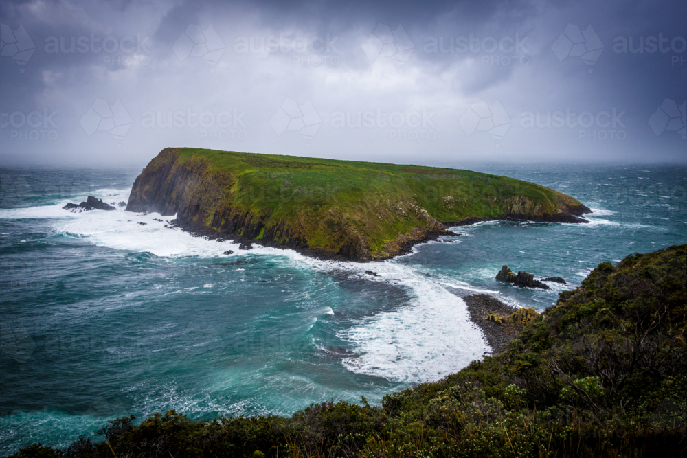 Stormy seas surround the rugged green slopes of Courts Island off the coast of Tasmania - Australian Stock Image