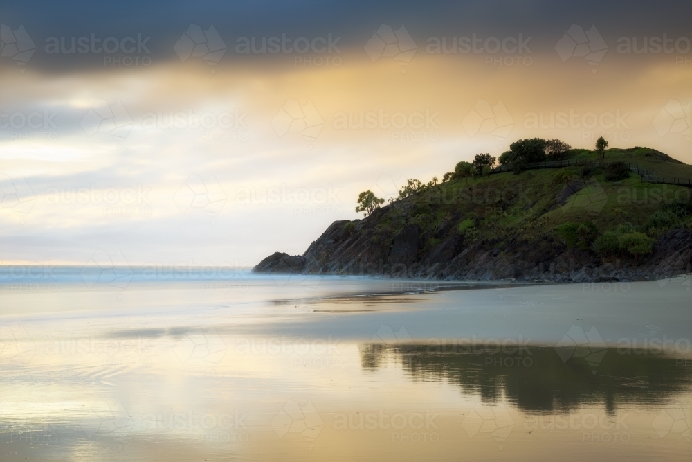 Stormy sunrise, beach reflections, and a coastal headland. - Australian Stock Image