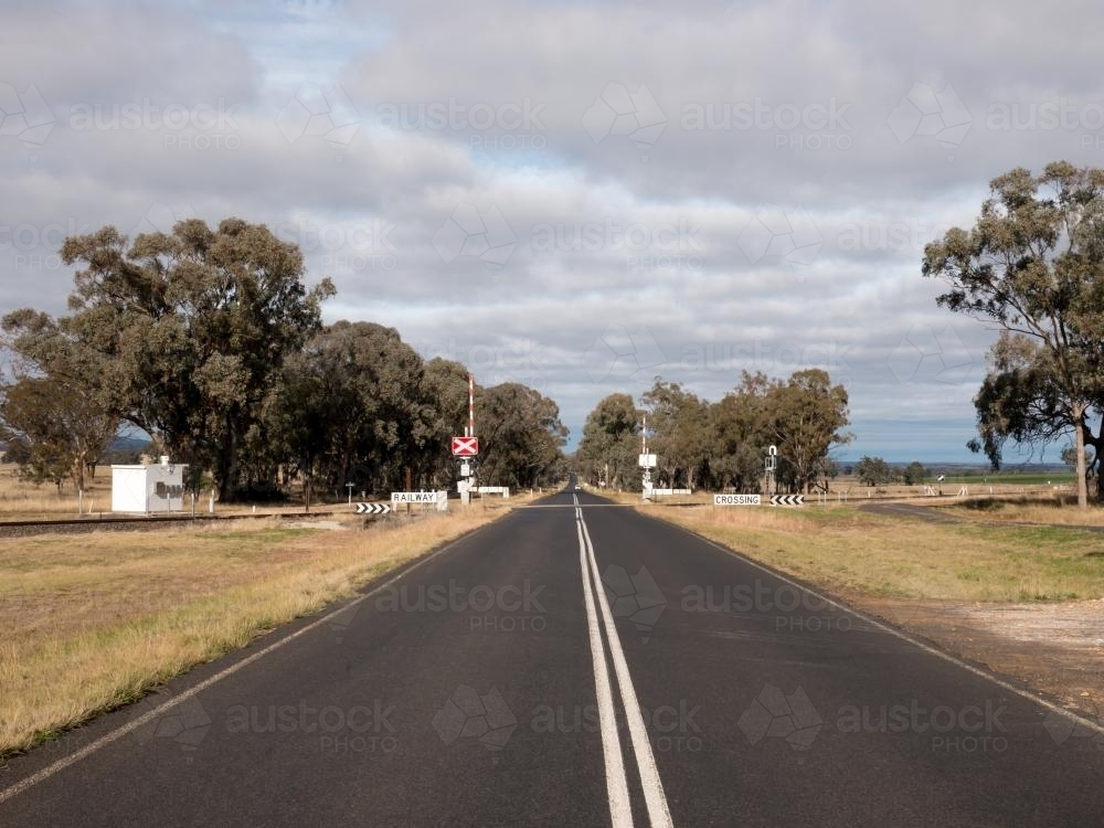 Straight bitumen road with double white lines and level crossing - Australian Stock Image