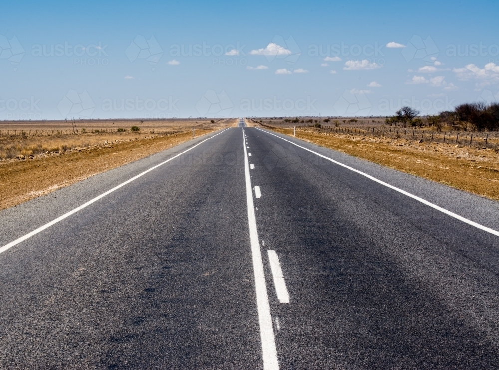 Straight bitumen road with white lines to horizon through drought stricken flat country - Australian Stock Image