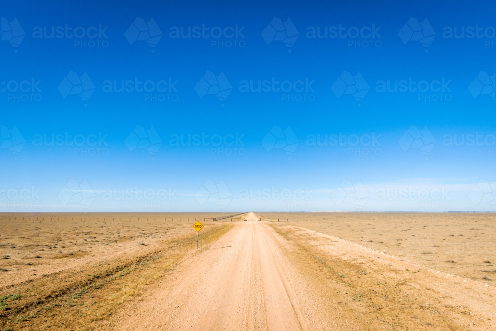 Straight dirt road through flat arid plains under clear blue sky - Australian Stock Image