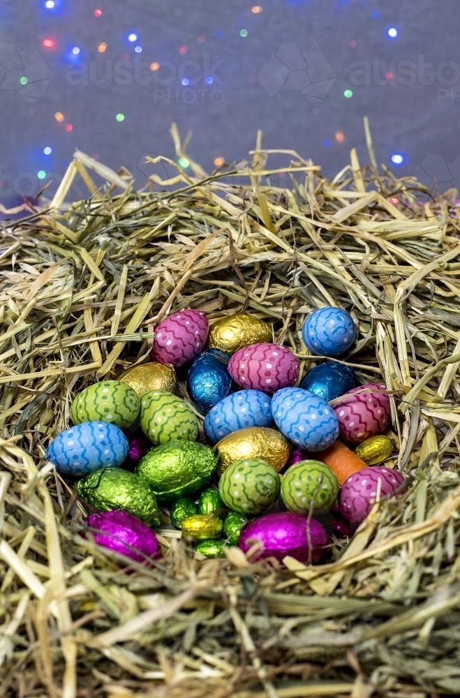 Straw nest filled with colourful easter eggs with coloured lights in background - Australian Stock Image