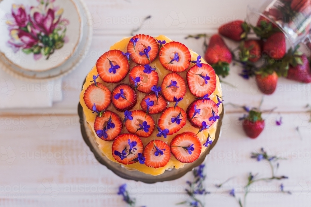 strawberries cut into rounds atop a sponge cake with lemon curd and edible flowers - Australian Stock Image