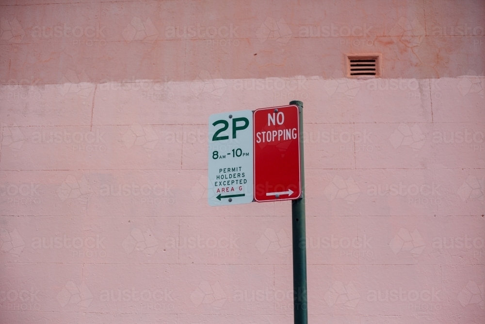 Street parking signs against pink wall - Australian Stock Image