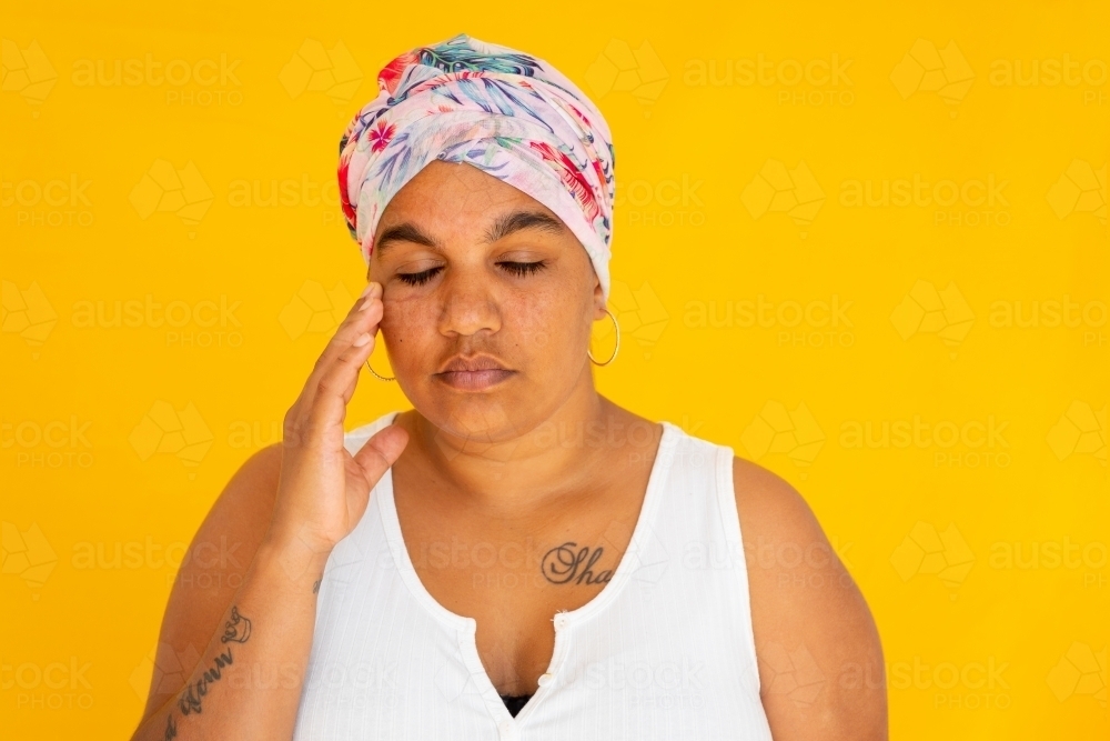 stressed woman with eyes closed and hand to face on yellow background - Australian Stock Image