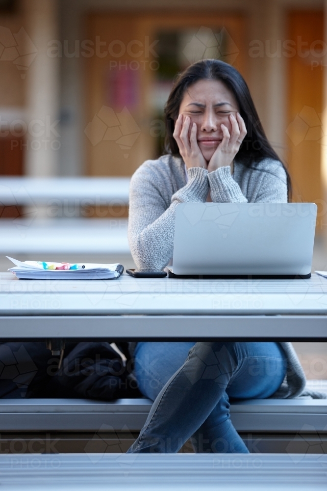 stressed Young Asian university student studying on laptop outdoors - Australian Stock Image