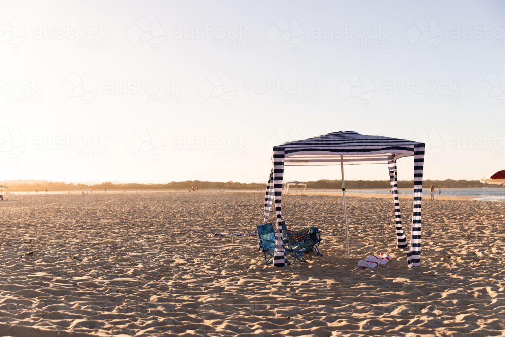 Striped navy‑and‑white canopy stands on the sandy shore - Australian Stock Image