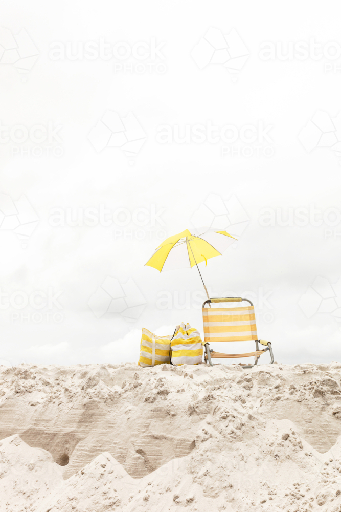 Striped white and yellow beach chair under matching umbrella on the beach - Australian Stock Image
