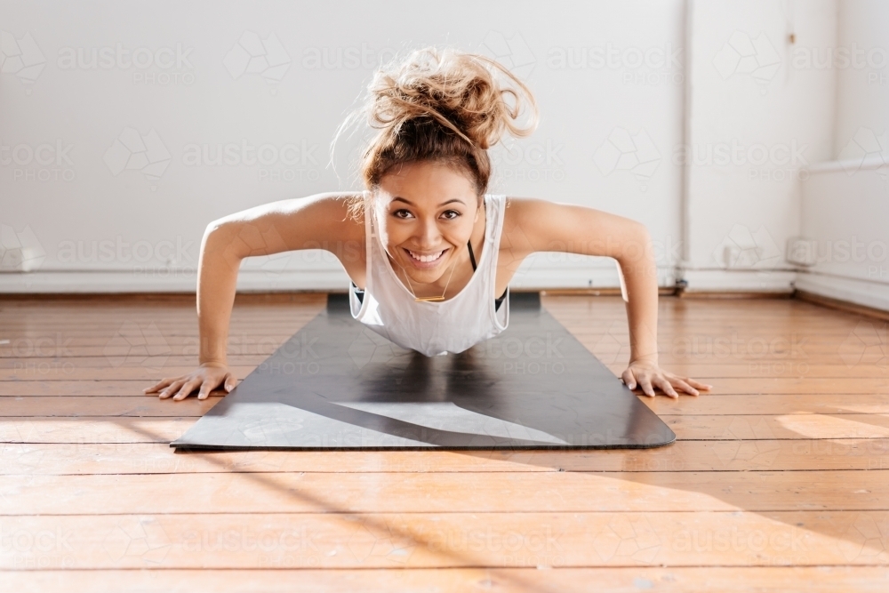 Strong young girl doing a push up and smiling - Australian Stock Image