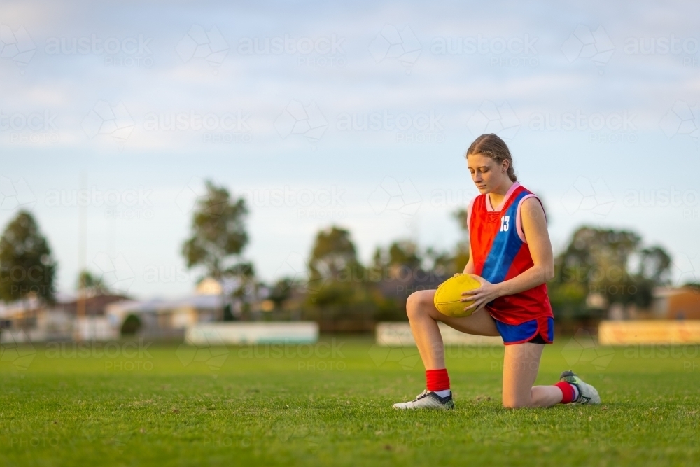 student football player kneeling on football field holding ball - Australian Stock Image