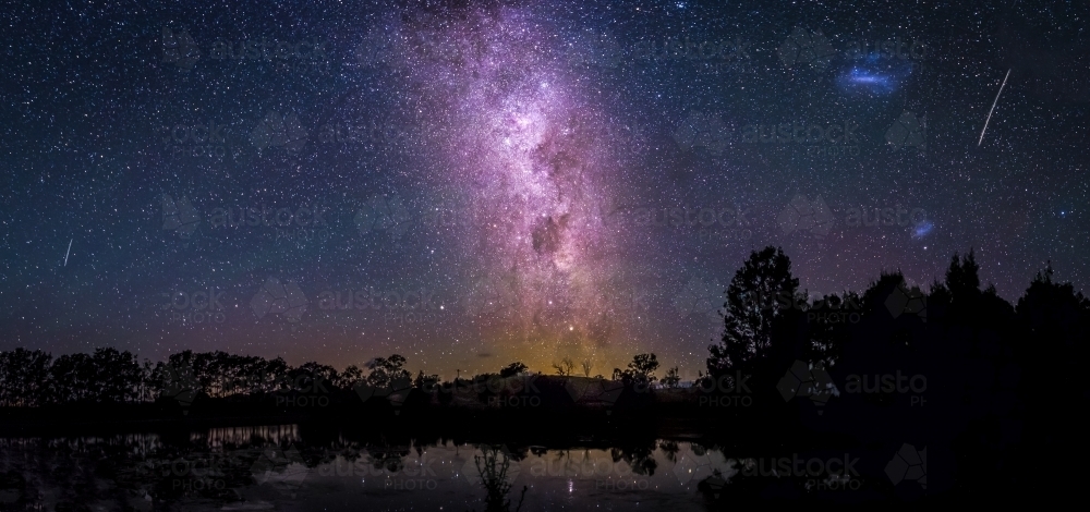 Stunning view of purple milky way over trees and lake - Australian Stock Image
