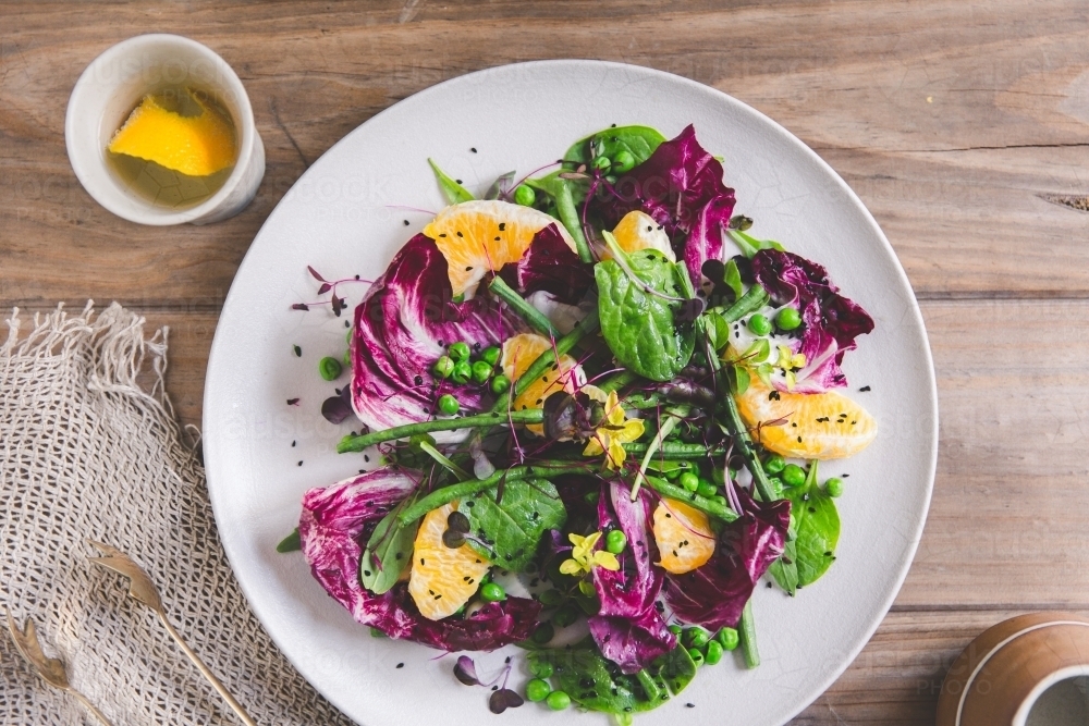 Overhead shot of a vibrant, raw vegan salad on styled timber table - Australian Stock Image