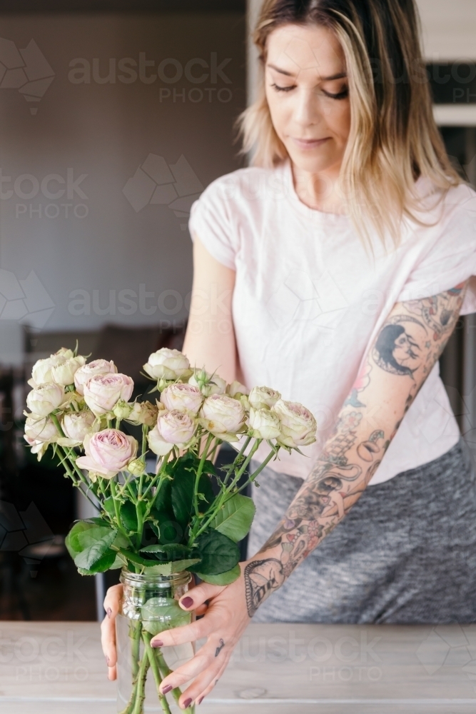 Stylist placing a vase of pink roses as a table centre piece - Australian Stock Image