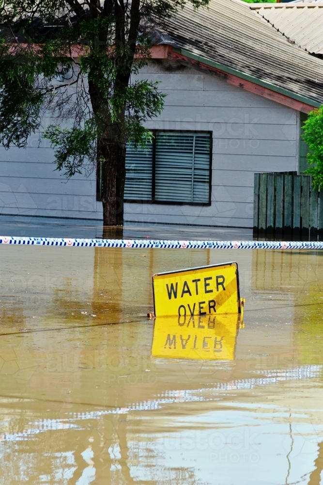 Submerged flood sign reading "water over road" - Australian Stock Image