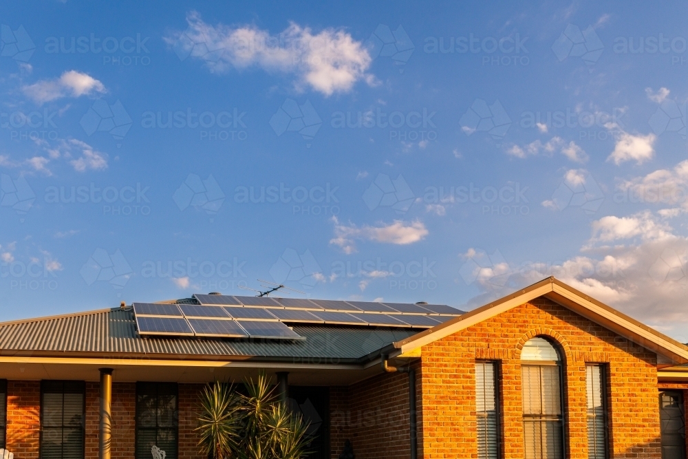 Suburban house with last sunset light of the day on bricks and solar panels installed on roof - Australian Stock Image
