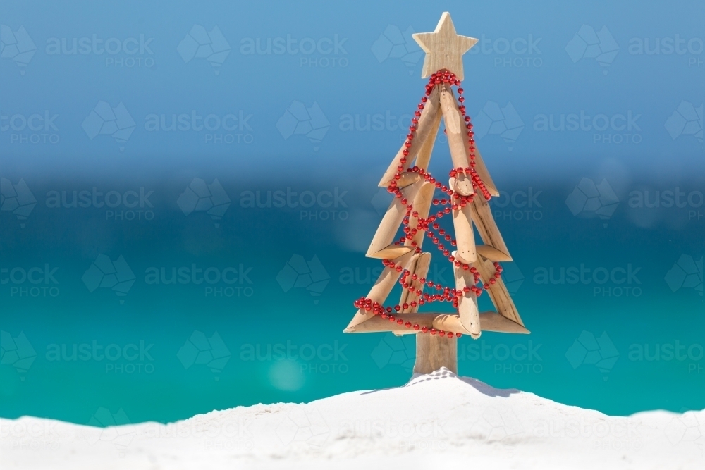 Summer sun shines down on a driftwood Christmas tree decorated with a string of red baubles - Australian Stock Image