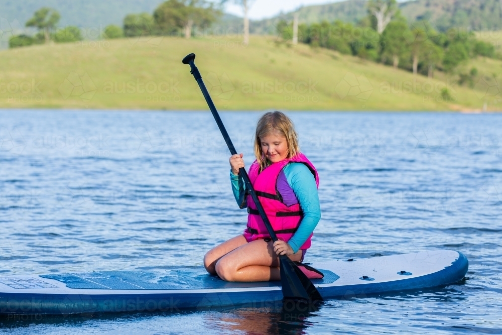 Summertime water fun with tween girl paddling on paddle board on lake - Australian Stock Image