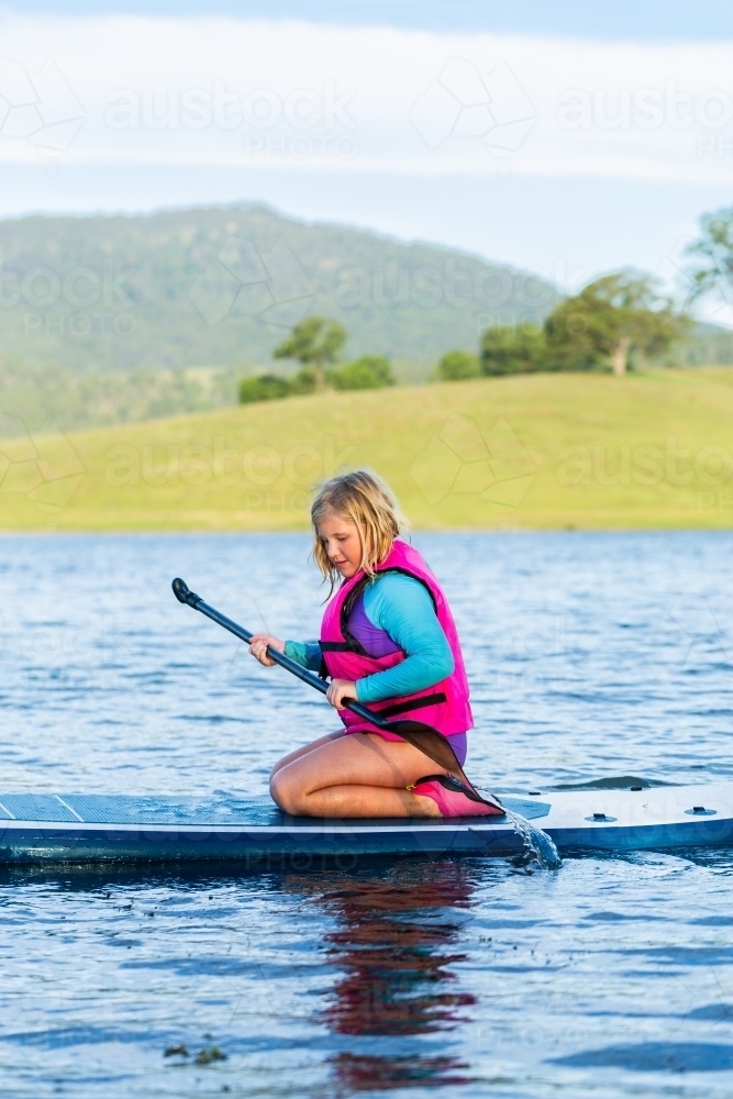 Summertime water fun with tween girl paddling on paddle board on lake - Australian Stock Image