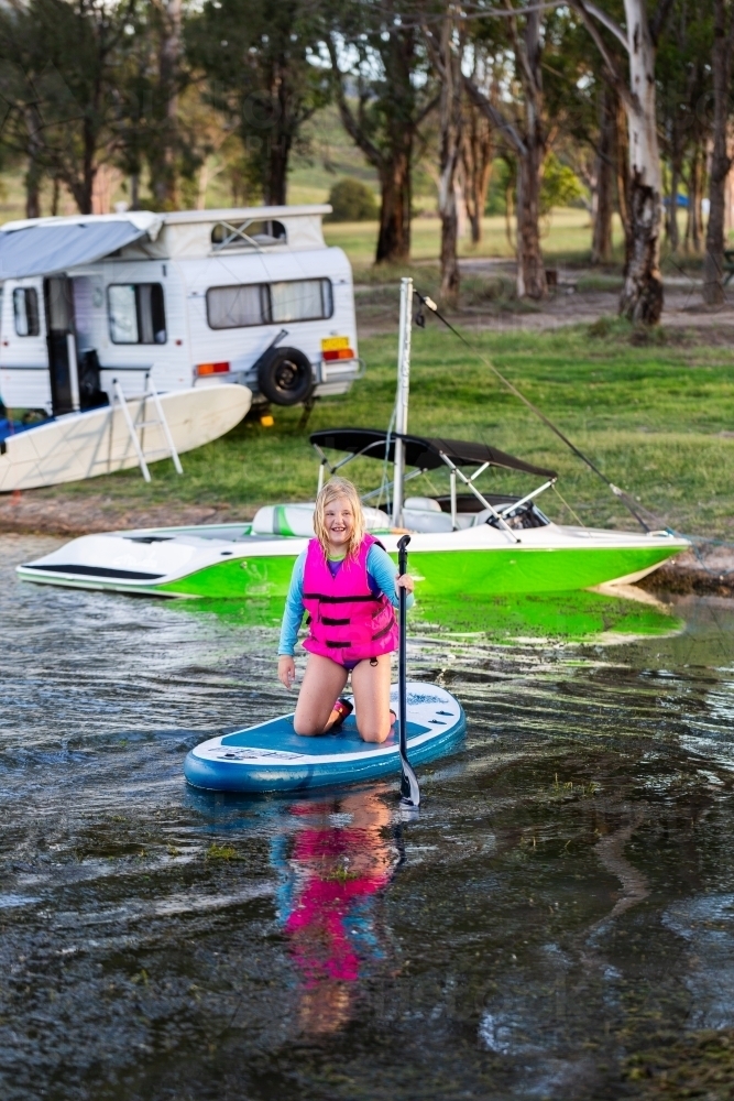 Summertime water fun with tween girl paddling on paddle board on lake - Australian Stock Image