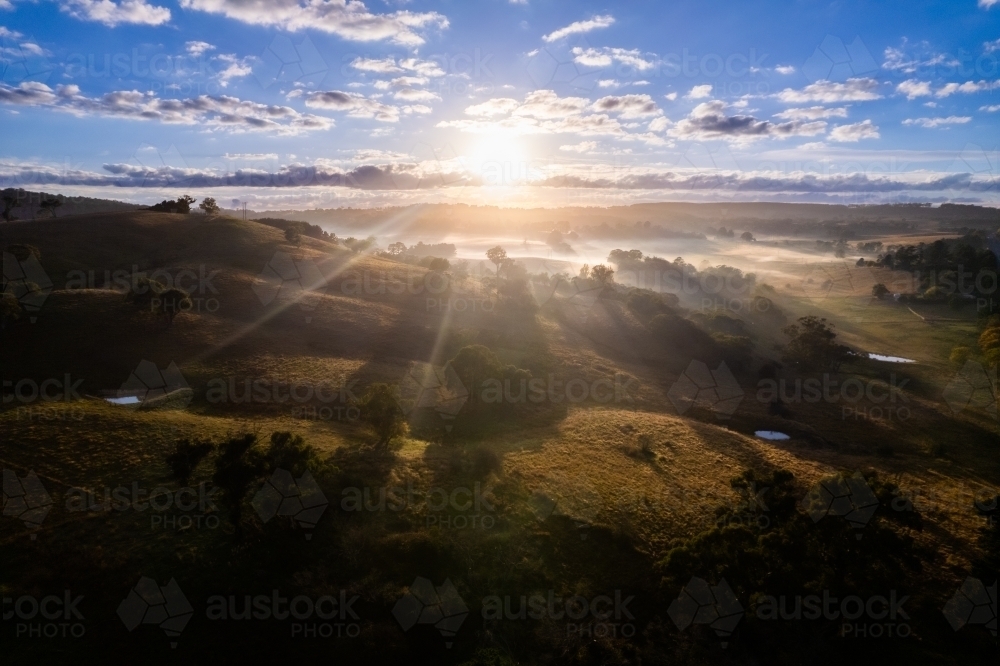 Sun beams streaking through the fog and trees onto the countryside below - Australian Stock Image