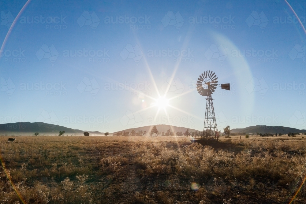 Sun flare behind old farm windmill on misty morning - Australian Stock Image