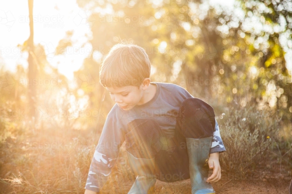 Sun flare over child playing in the dirt - Australian Stock Image