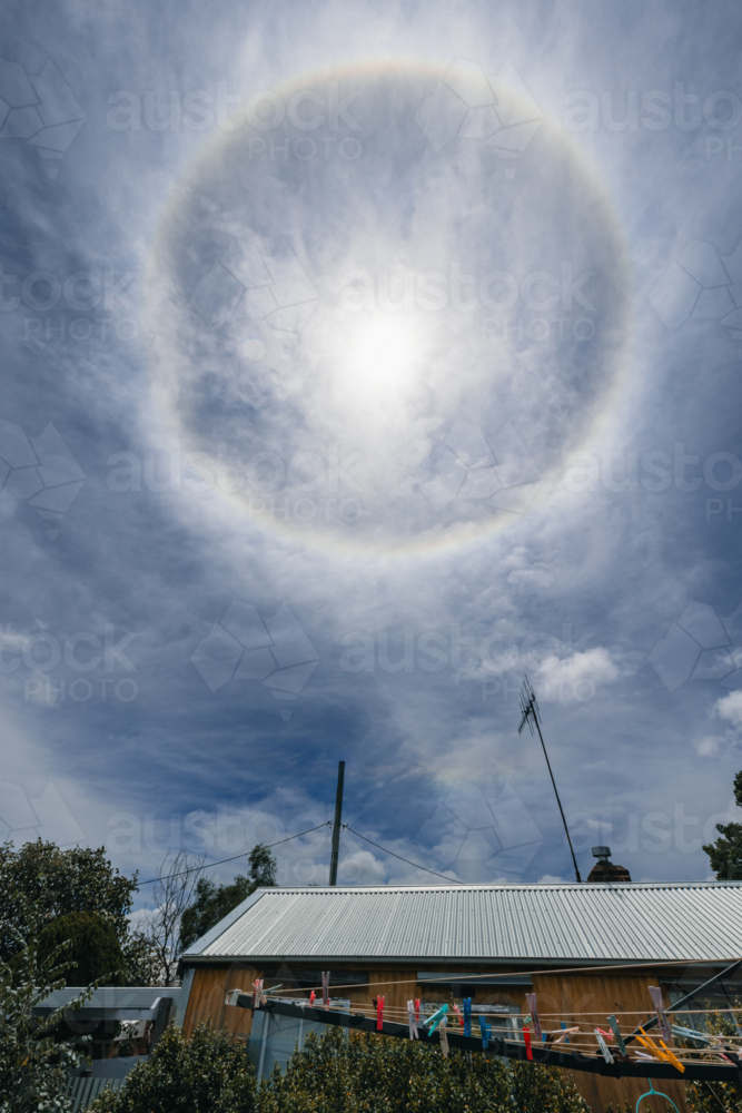 Sun halo optical phenomenon in a cloudy sky above a suburban rooftop - Australian Stock Image