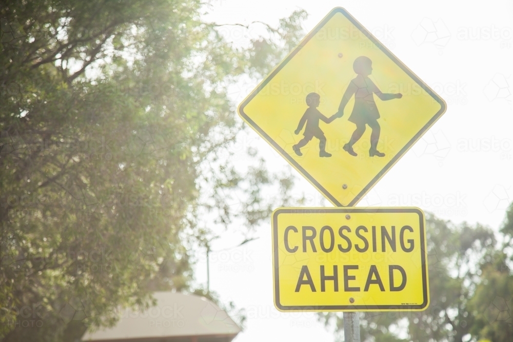 Sun haze over crossing ahead sign beside road near school - Australian Stock Image