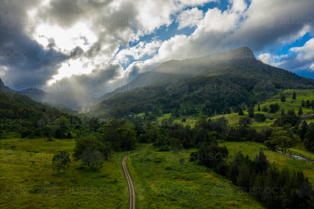 Sun rays coming through clouds over hilly landscape. - Australian Stock Image