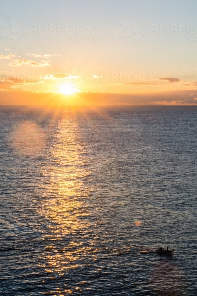 Sun reflecting on water with boat in foreground during sunrise - Australian Stock Image