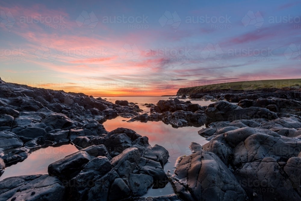 Sun rising over rocks and water at Kiama - Australian Stock Image