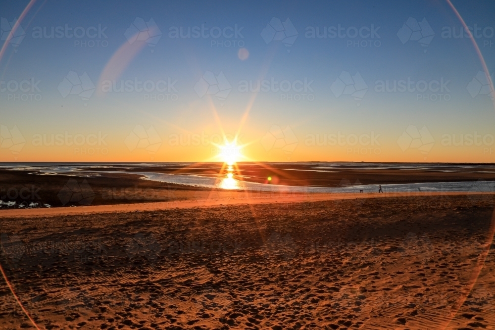 Sun rising through blue sky over ocean channel and sandy coastline - Australian Stock Image
