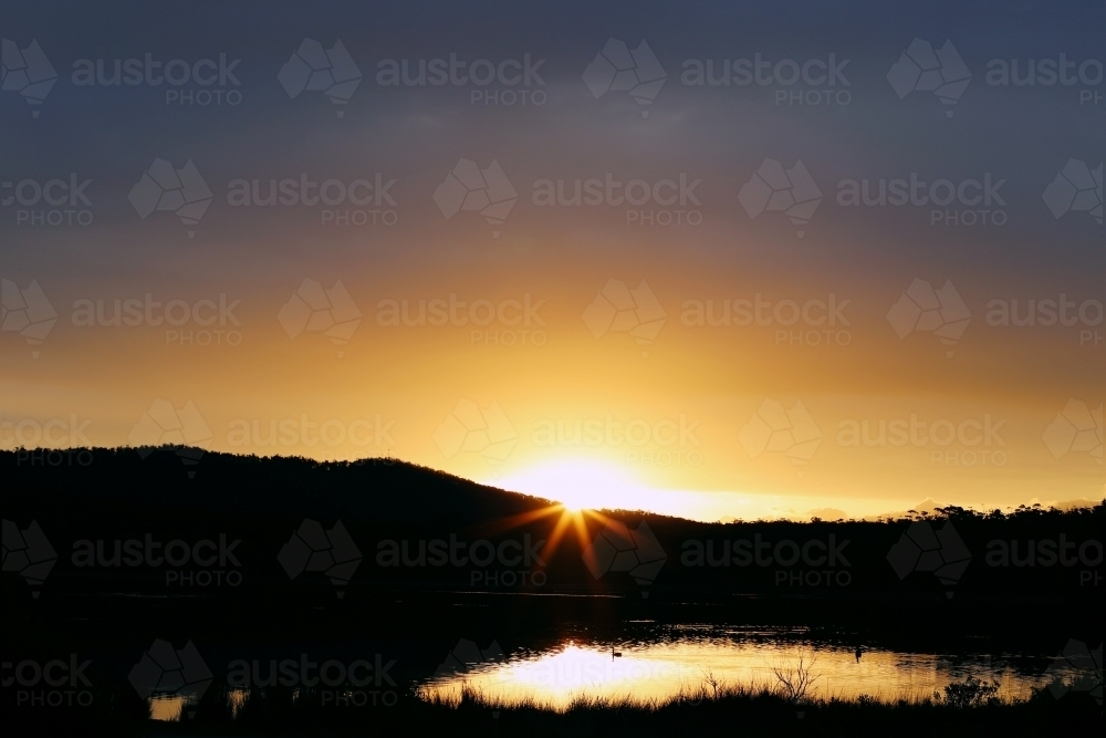 Sun setting behind a mountain - Australian Stock Image