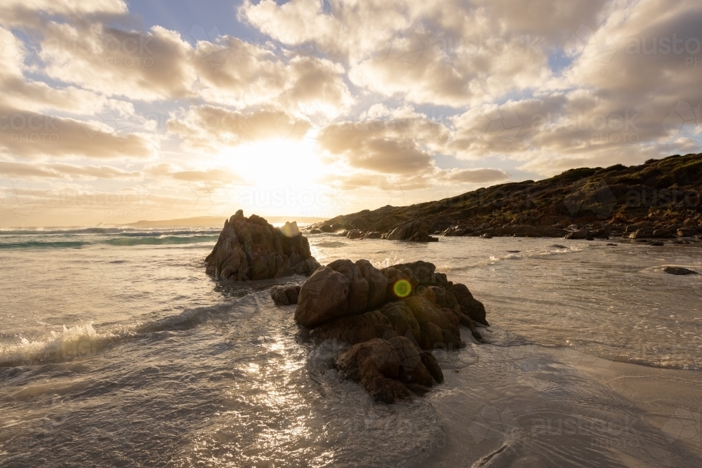 sun setting behind rocks on south coast beach - Australian Stock Image