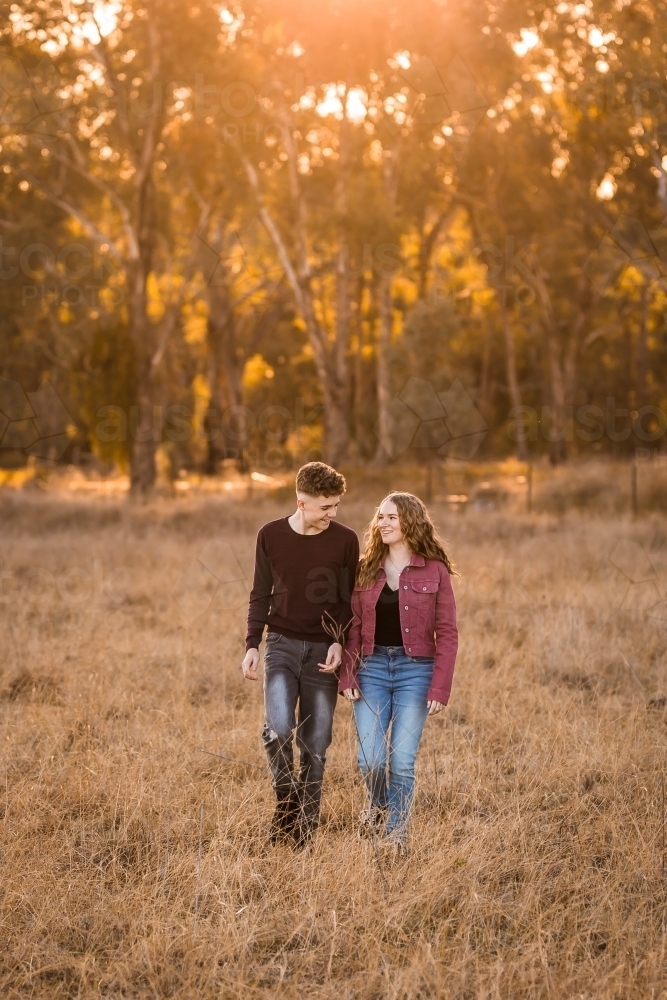 Sun shining on two youth walking through paddock with trees in background - Australian Stock Image