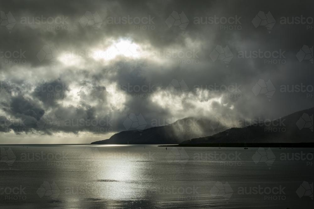 Sun shining through the clouds onto ocean and mountain : Austockphoto Sun shining through the clouds onto ocean and mountain - Australian Stock Image