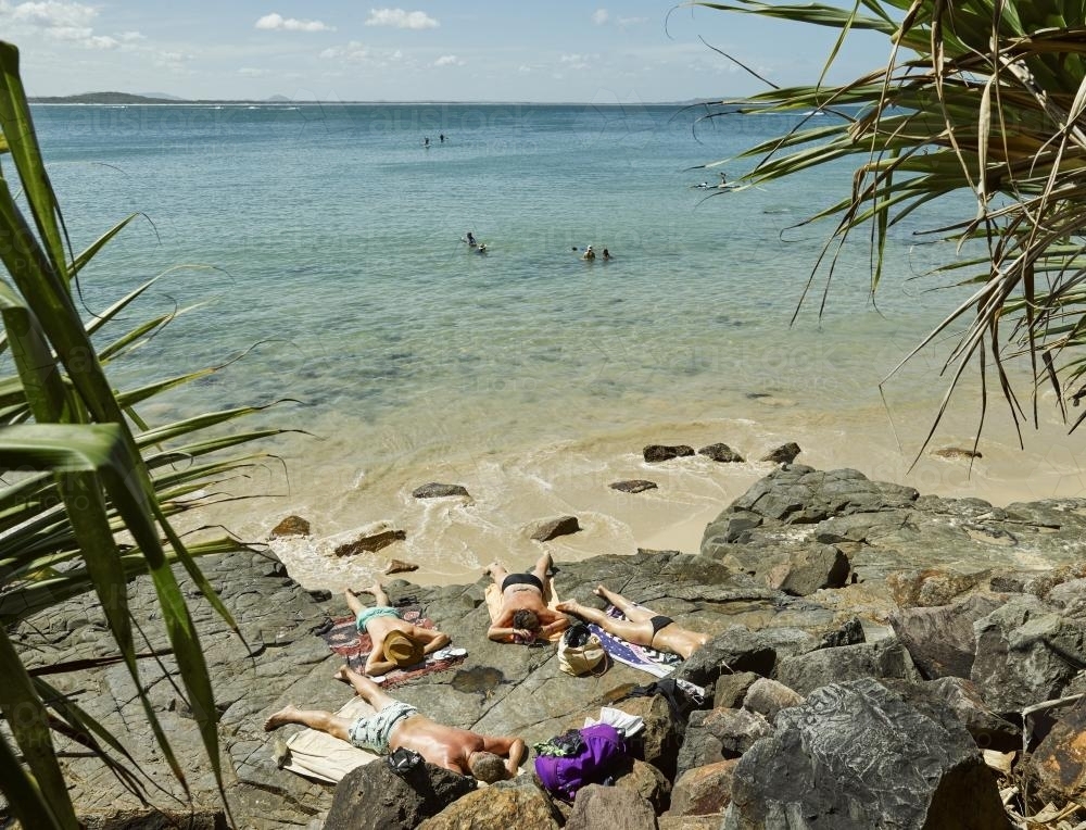 Sunbathers on rocks beside the beach - Australian Stock Image