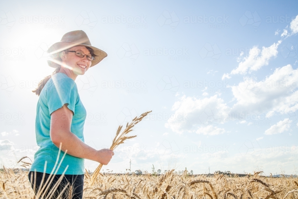 Sunflare behind a happy farm girl holding a sheaf of bearded wheat - Australian Stock Image
