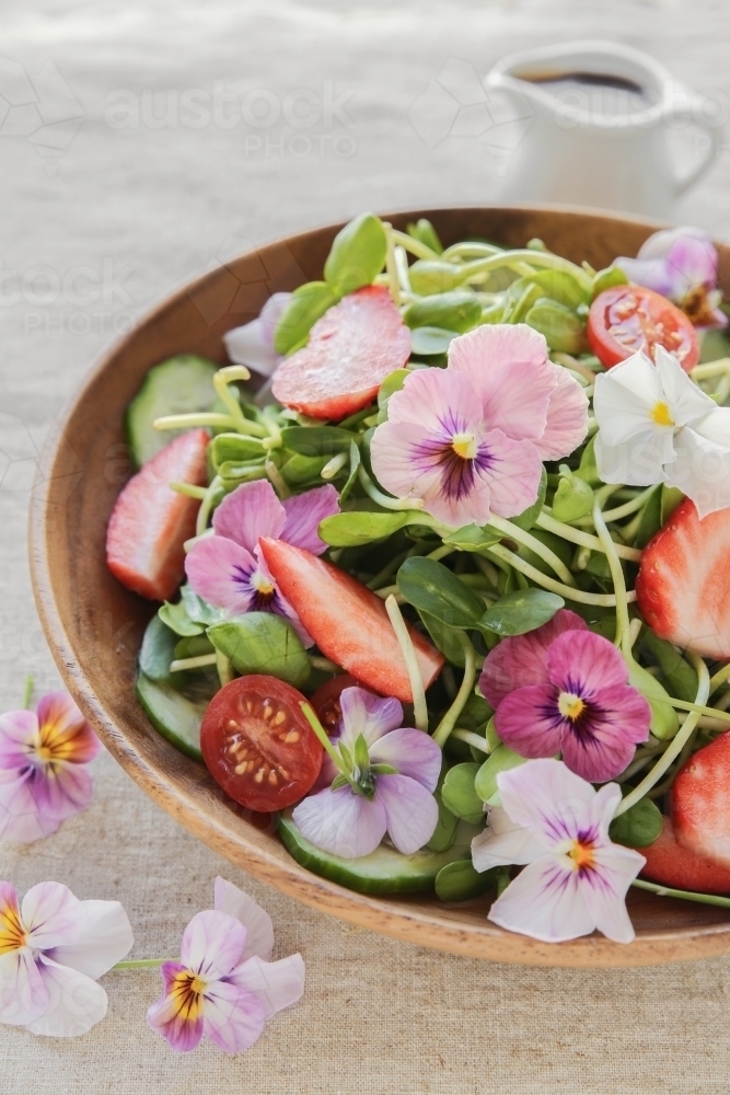 Sunflower sprouts, cucumber and edible flowers salad on wooden bowl - Australian Stock Image