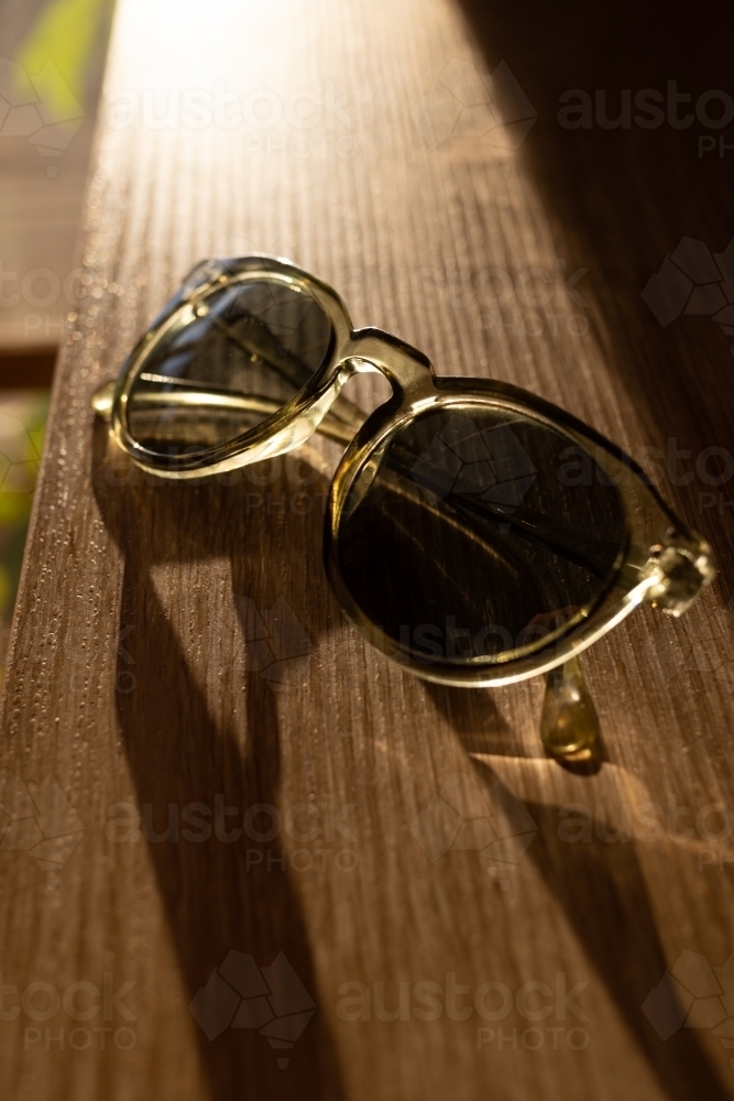 Sunglasses sitting on a timber table in the afternoon light - Australian Stock Image