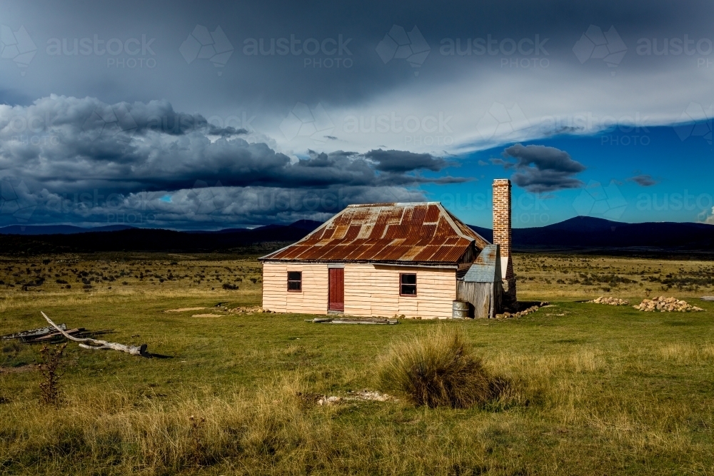 Sunlight and storms at an old hut in Snowy Mountains, Kosciuszko National Park - Australian Stock Image